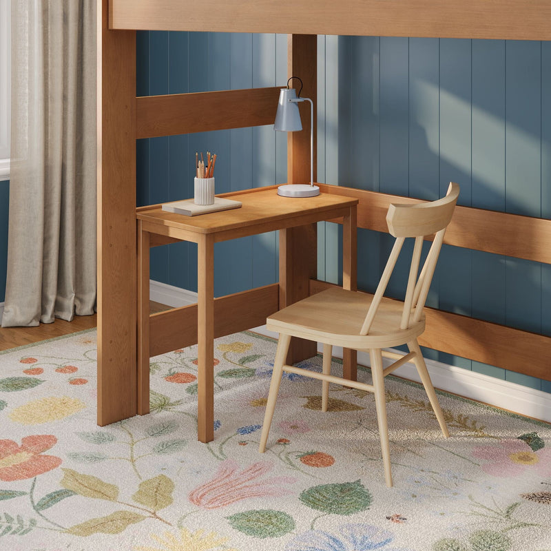 Kids loft bed study nook with wooden desk and chair, blue paneled wall, white desk lamp, pencil cup and pastel floral rug