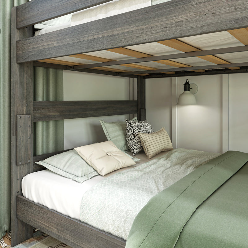 Gray rustic wooden bunk bed with sage green bedding, patterned throw pillows, visible slatted bed base and wall-mounted bedside lamp in cozy bedroom