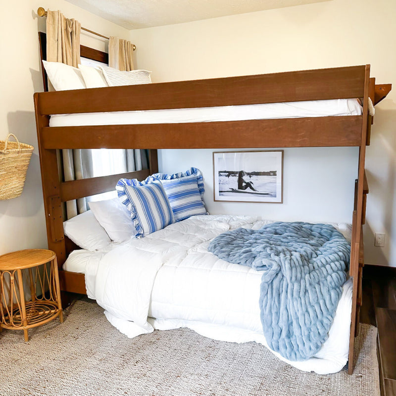 Wooden bunk bed in coastal-style bedroom with white comforter, blue striped pillows, plush blue throw and wicker accent decor