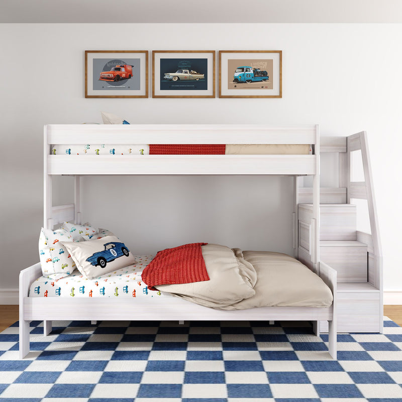 White wooden twin-over-twin bunk bed with staircase and built-in storage, car-print kids bedding, red throw and framed vintage car wall art over blue checkered rug in modern children's bedroom