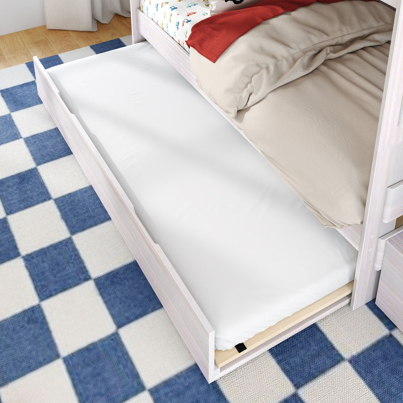 White wooden pull-out trundle bed with mattress under bunk bed on blue checkered rug — space-saving kids bedroom extra sleeping solution