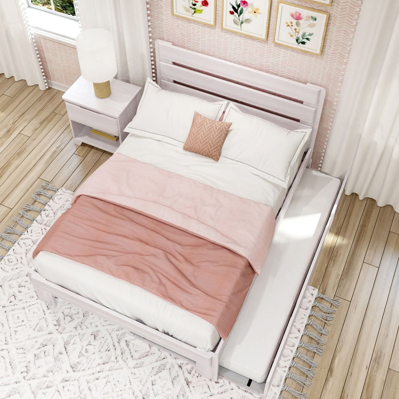 Pink and white bedroom with white wooden platform bed, soft pink duvet and textured accent pillow, white nightstand with gold lamp, floral wall art, hardwood floor and patterned rug