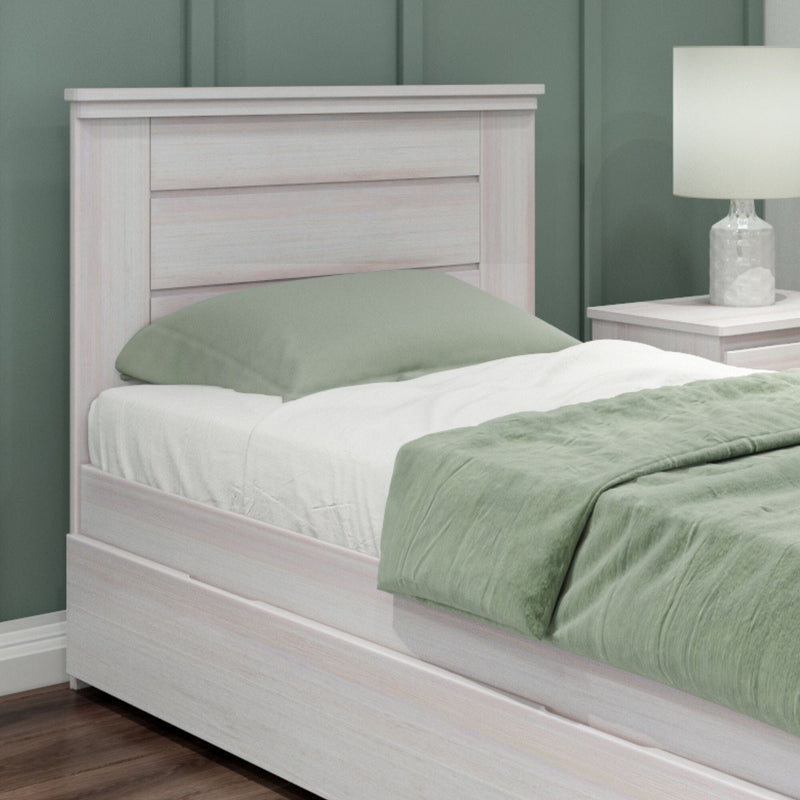 Whitewashed wood bed frame with slatted headboard, sage green bedding and matching nightstand with lamp in a modern bedroom