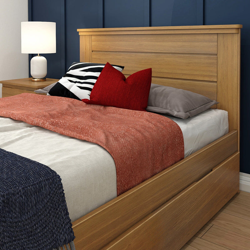Modern oak bed frame with storage drawers, paneled headboard, coral quilt, red accent pillows and white bedside lamp