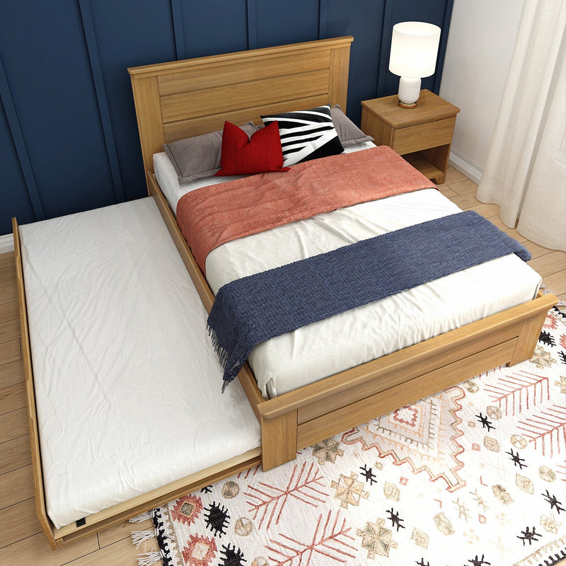 Wooden trundle bed against a navy paneled accent wall with red and black decorative pillows, coral throw and navy runner, oak nightstand with lamp and boho patterned rug