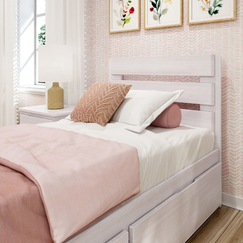 Pastel pink bedroom with white wooden twin bed and trundle, blush knit throw pillow, white bedside lamp, floral wall art and natural window light