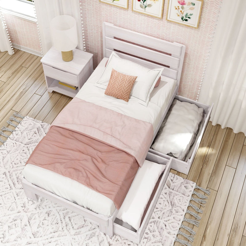 Cozy pastel pink girls bedroom with white wooden bed, nightstand and lamp, decorative floral wall art, pink bedding and pull-out storage trundle