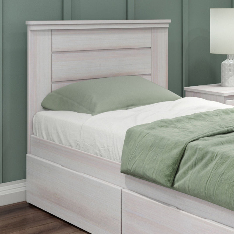 Whitewashed wood twin bed with built-in under-bed storage drawers, sage green duvet and pillow, bedside table with lamp against green paneled accent wall