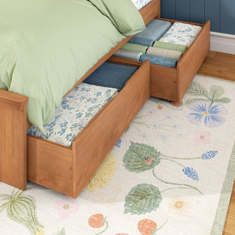 Wooden platform bed with pull-out under-bed drawers storing folded linens and quilts, green bedspread and floral rug for space-saving bedroom storage