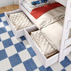 White wooden bunk bed with two pull-out underbed storage drawers, beige bedding and car-print pillow on blue checkered rug in kids' bedroom