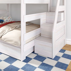 White wooden twin-over-twin bunk bed with built-in staircase storage and drawers, beige bedding and blue checkered rug in kids' bedroom.