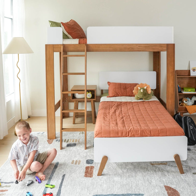Wooden loft bunk bed in a bright kids' bedroom with ladder, rust-orange bedding, plush dinosaur, toy cars on a patterned rug and a child playing near a floor lamp