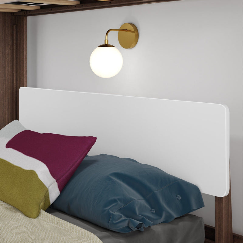 Modern brass wall sconce above white headboard in a minimalist bedroom with colorful pillows and navy duvet