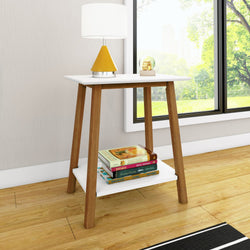 Mid-century modern side table with wooden legs, white top, and lower shelf holding books, placed in a bright living room by a large window.