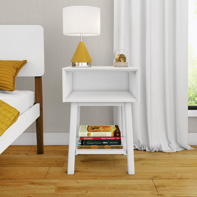 Minimalist white bedside table with mustard yellow table lamp, stacked books on lower shelf, white curtains and hardwood floor in modern Scandinavian bedroom interior