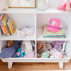Kids' bookshelf with colorful children's books, pink cap, unicorn slippers, and plush toys.