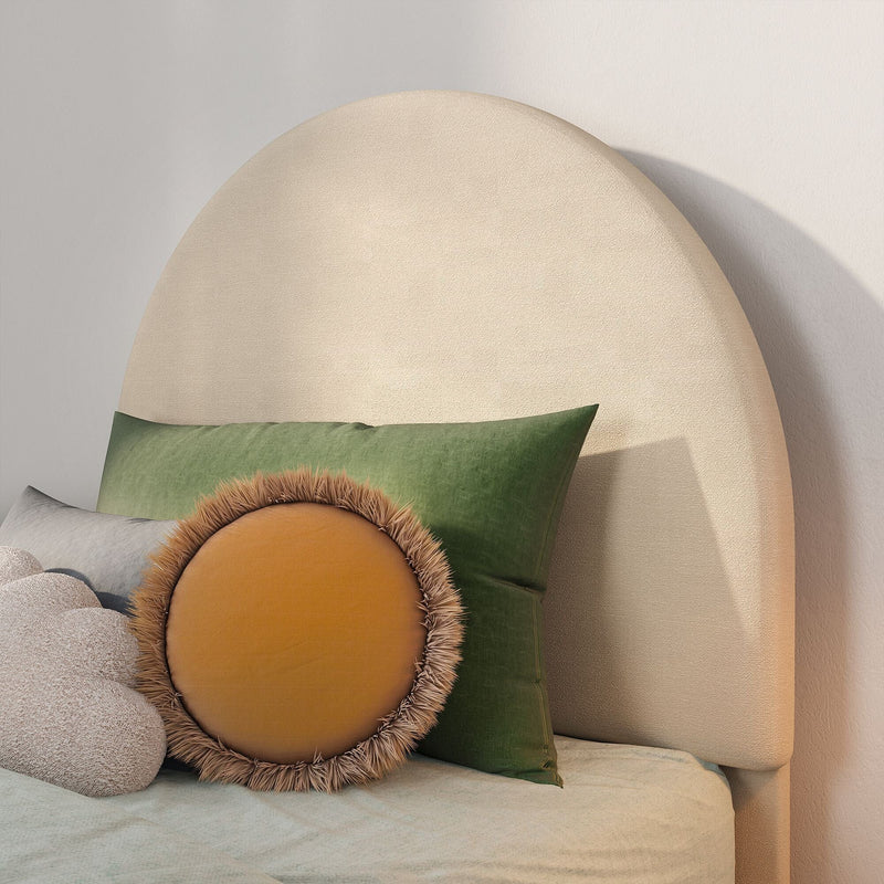Beige upholstered rounded headboard with green velvet pillow and round mustard fringe cushion on a cozy modern minimalist bed