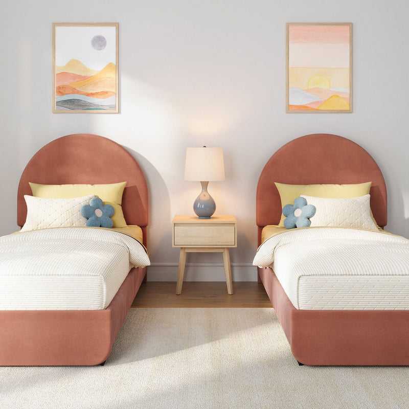 Modern kids' twin bedroom with coral rounded headboards, yellow bedding and blue flower pillows, wooden nightstand with ceramic lamp, pastel abstract wall art and soft beige carpet