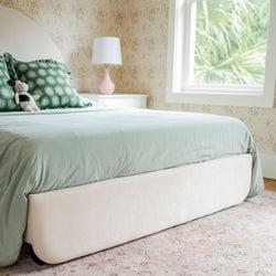 Stylish bedroom with green bedding, decorative pillows, and soft lighting, featuring a modern bedside lamp and window view.