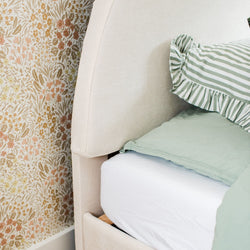 Elegant bedroom with floral wallpaper, cushioned beige headboard, and striped green bedding.