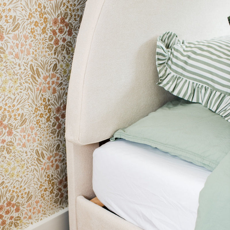 Close-up of beige upholstered headboard with vintage floral wallpaper and mint green striped ruffle pillow, bedroom decor