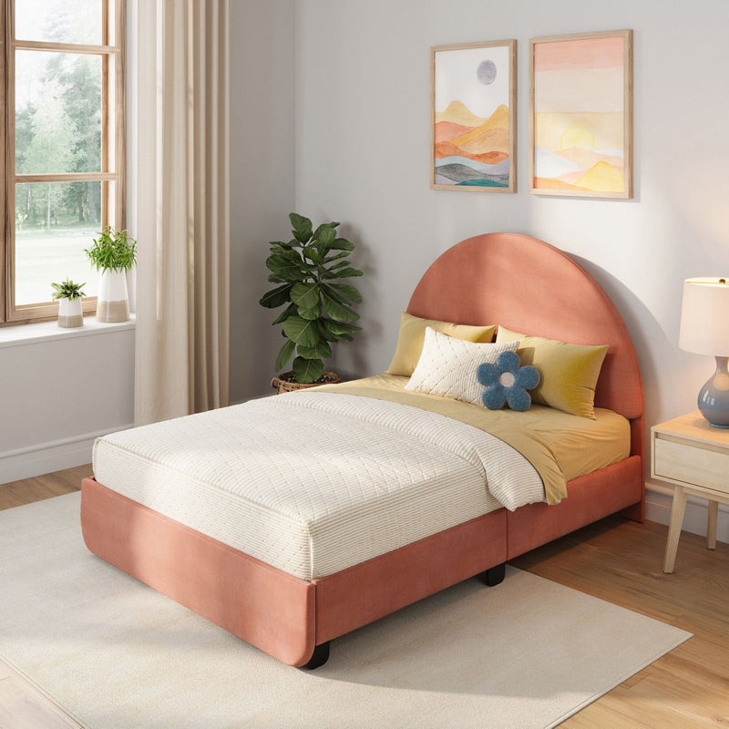 Sunlit modern bedroom with coral upholstered bed, neutral quilted bedding, decorative pillows including a blue flower cushion, potted plants, and pastel framed landscape wall art