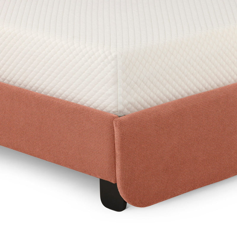 Close-up of quilted white mattress corner on coral textured upholstered bed frame showing fabric detail and black leg