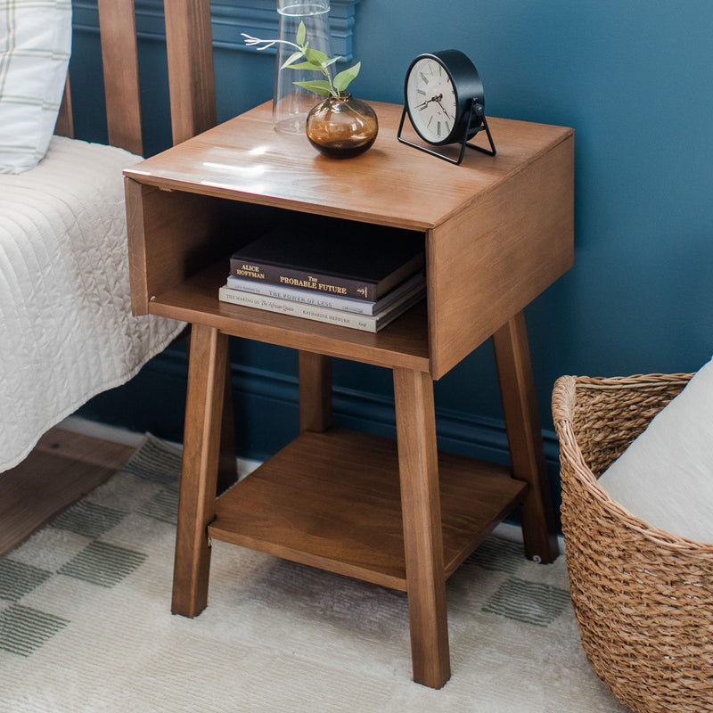 Wooden bedside table nightstand in blue bedroom with vintage tabletop clock, amber vase with greenery, stacked books and woven basket