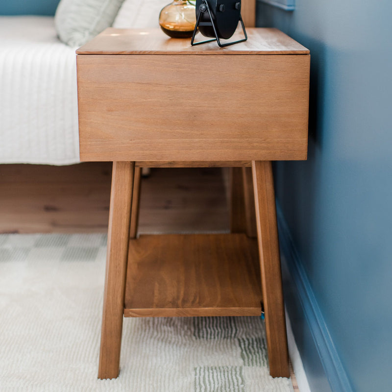 Light oak mid-century modern bedside table (nightstand) with black lamp and amber glass vase against blue accent wall