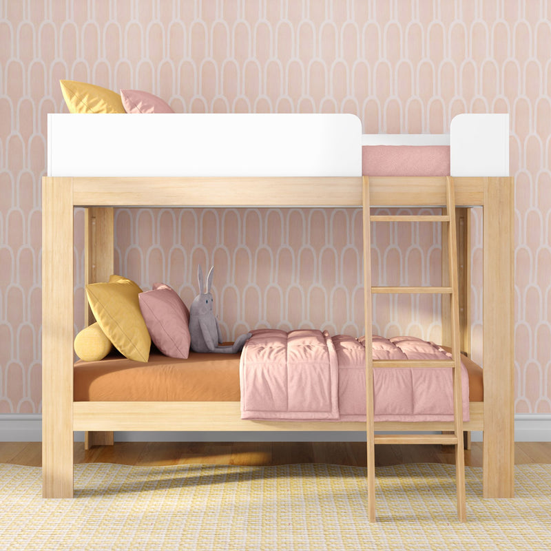 Wooden loft bunk bed with ladder in pink pastel nursery, styled with blush bedding, yellow accent pillows and a gray stuffed bunny.