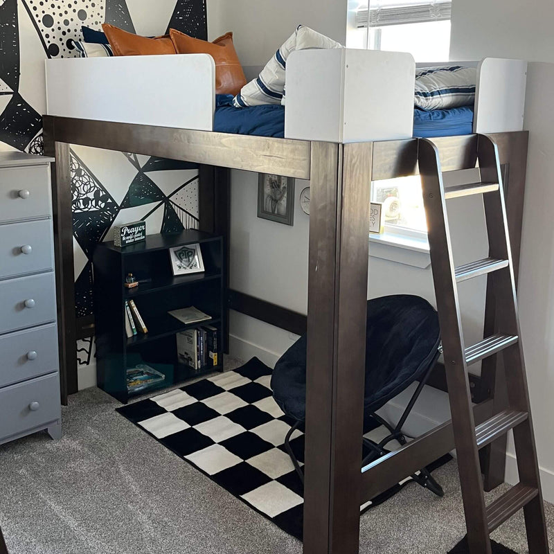 Modern wooden loft bed with ladder and white guardrails, navy bedding and leather accent pillows above a bookshelf, black-and-white geometric wall mural and checkerboard rug in kids' bedroom
