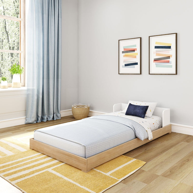 Modern children's bedroom with low wooden platform bed, light blue bedding and curtains, yellow rug, wicker basket and framed abstract art