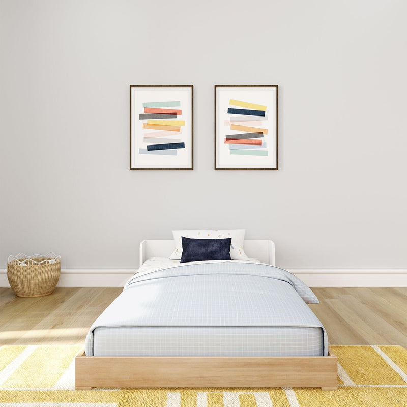 Minimalist kids' bedroom with twin bed, light blue bedding and navy pillow, neutral gray wall, two modern abstract framed prints, rattan basket and yellow area rug.
