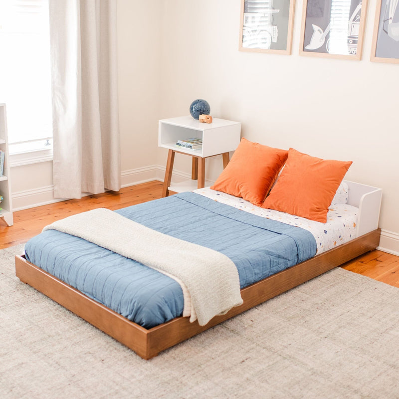 Modern kids' bedroom decor: wooden platform bed with blue quilt, orange pillows, white bedside table, framed wall art and hardwood floor