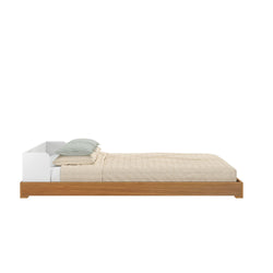 Minimalist wooden platform bed with beige bedding and green pillows, side view.