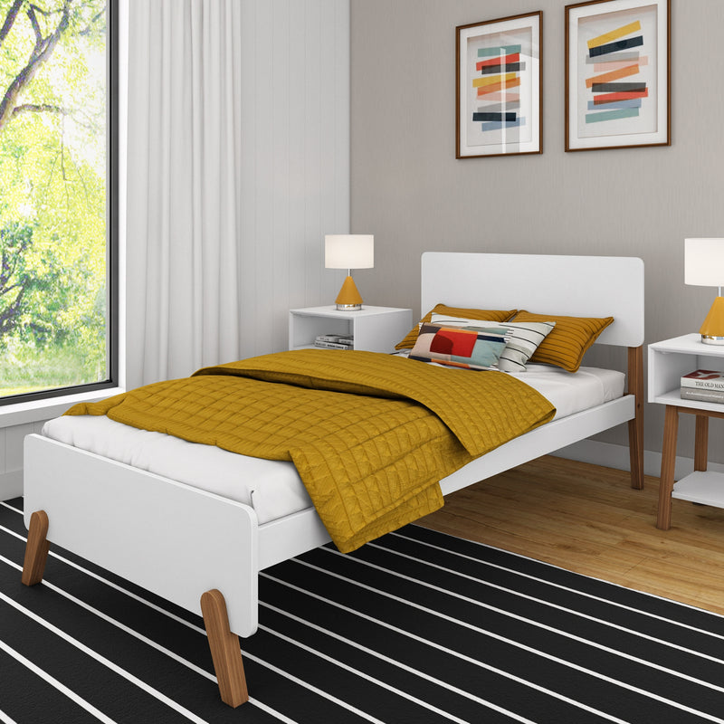 Modern minimalist bedroom with mustard yellow quilted bedding on a white platform bed, white bedside tables with yellow table lamps, abstract framed wall art, black-and-white striped rug and large window with leafy green view