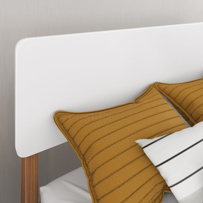 Close-up of modern white headboard with wooden legs, mustard quilted throw pillows and white striped accent pillow in a minimalist bedroom