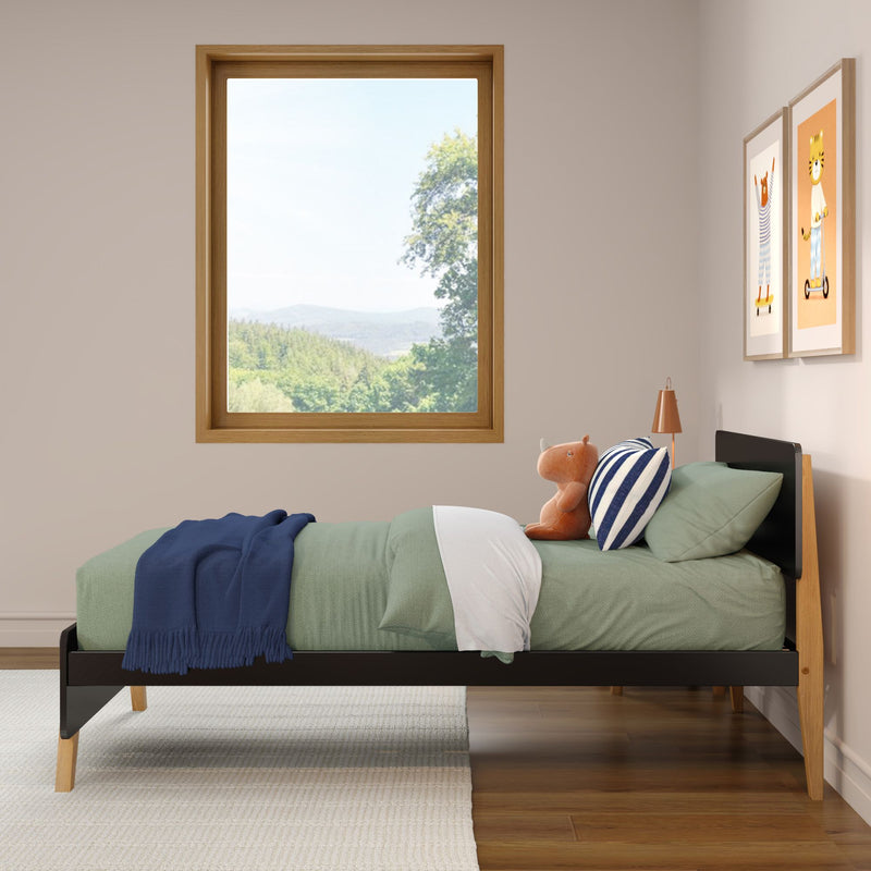 Children's bedroom with green twin bed, navy throw and striped pillow, plush toy on bed, wooden-framed window showing scenic forest view and animal wall art