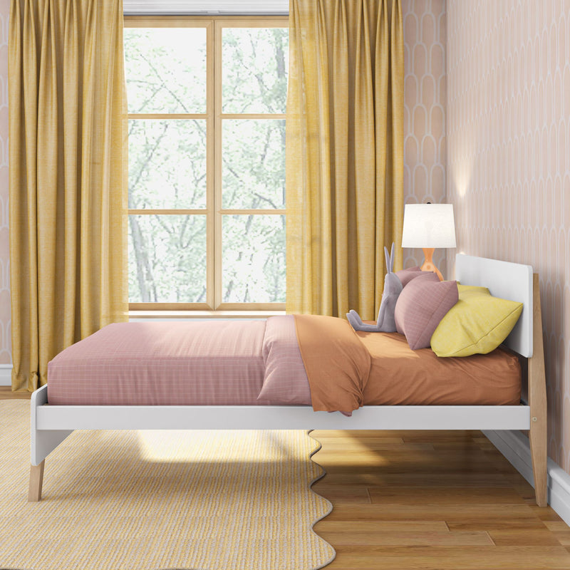Children's pastel bedroom with pink bedding, mustard-yellow curtains, scalloped area rug, wooden floor, bedside lamp and stuffed bunny