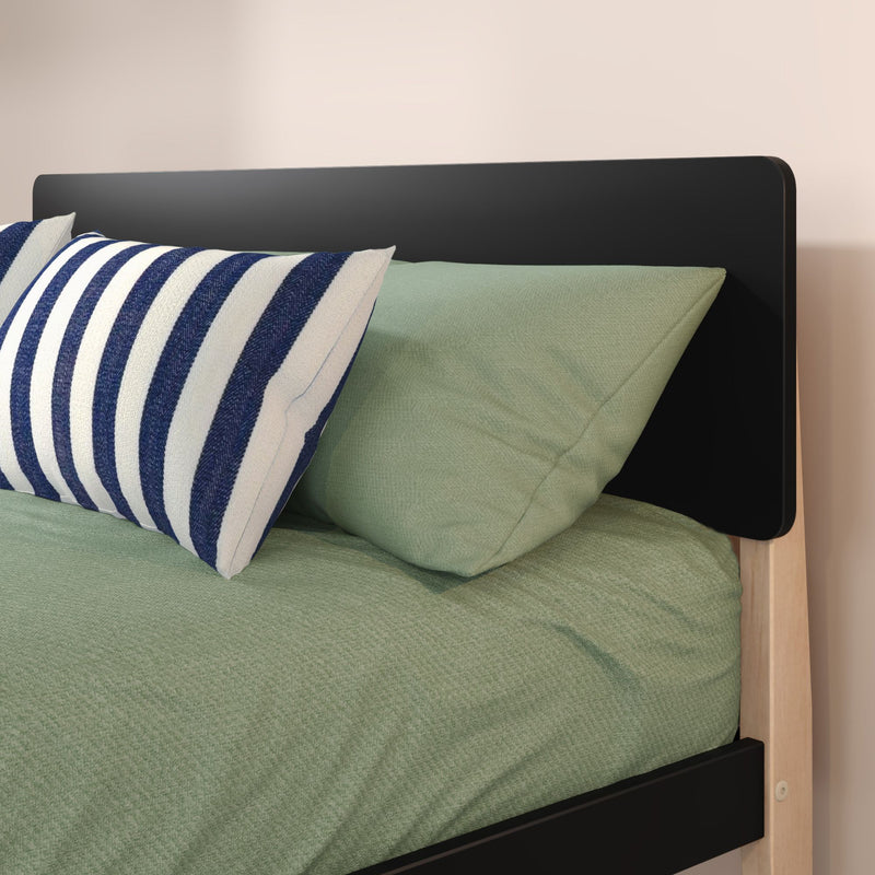 Close-up of modern bed with black headboard and light wood frame, sage green bedding and navy-and-white striped accent pillow, minimalist bedroom decor