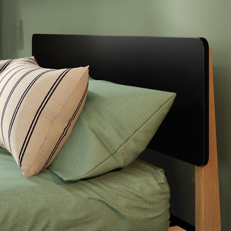 Minimalist bedroom close-up: black headboard on wooden bed frame, green textured bedding and beige striped pillow