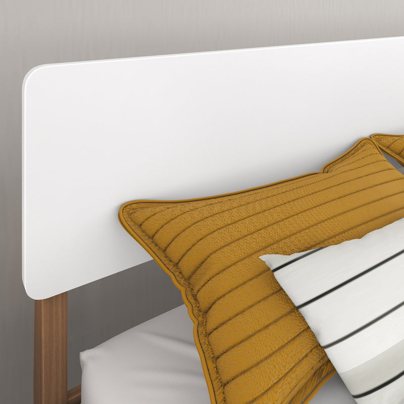 Minimalist bedroom close-up of a modern white headboard and walnut wood bed frame with mustard quilted pillow and striped gray wall
