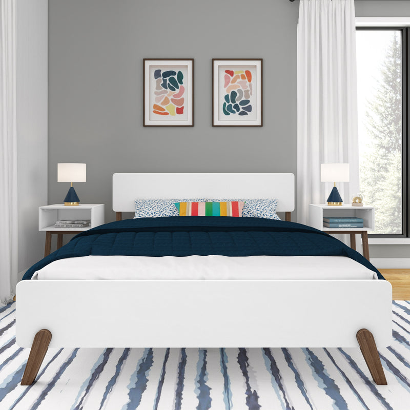 Modern bedroom with white platform bed, navy bedding, colorful striped accent pillow, framed abstract wall art, white nightstands and blue lamps