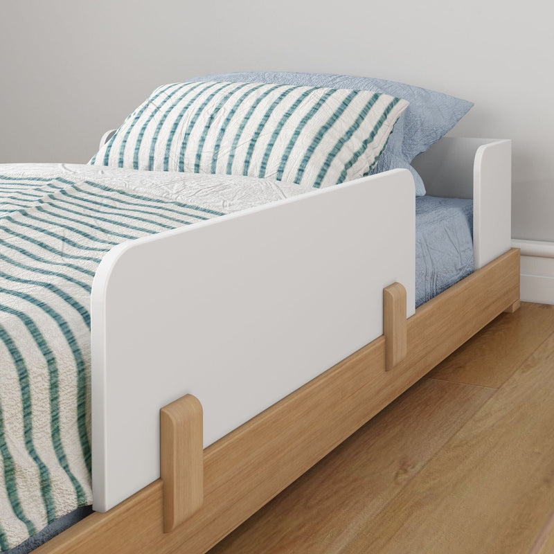 Toddler bed with wooden frame and safety rail on wooden floor.