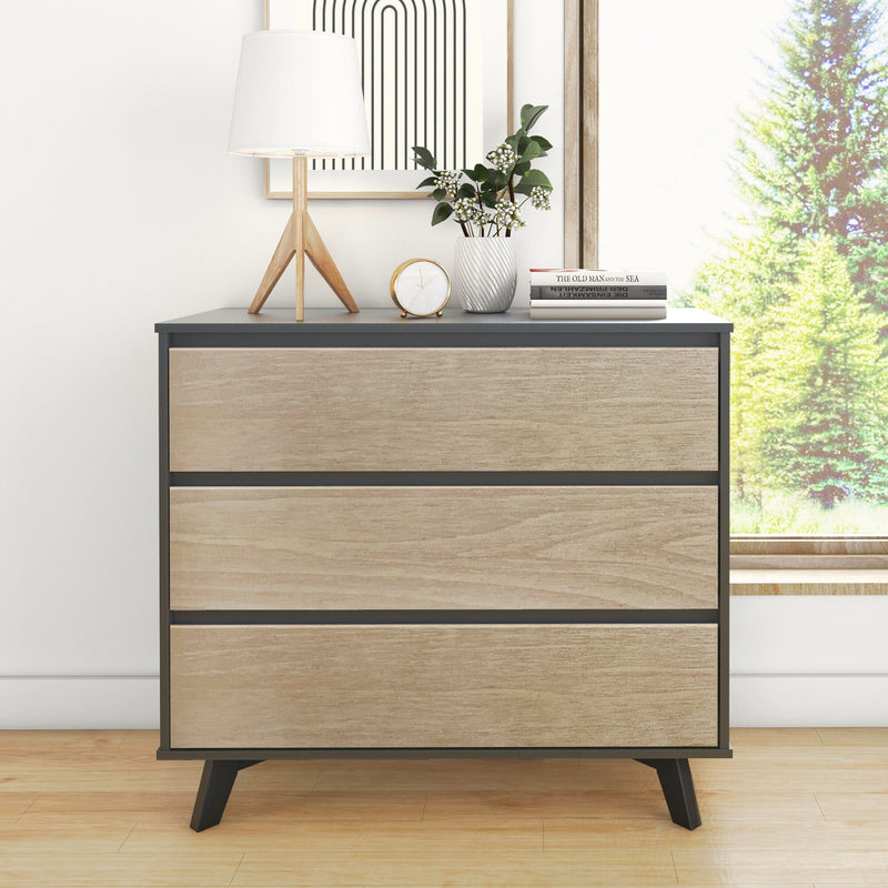 Mid-century modern three-drawer bedroom dresser in light oak with black frame, styled with a tripod lamp, clock, vase of greenery and books by a sunny window