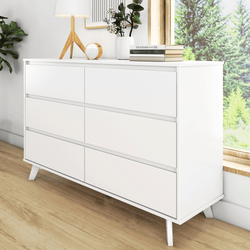 White modern dresser with six drawers in a bright room with wooden floor, indoor plant, books, and decorative items.