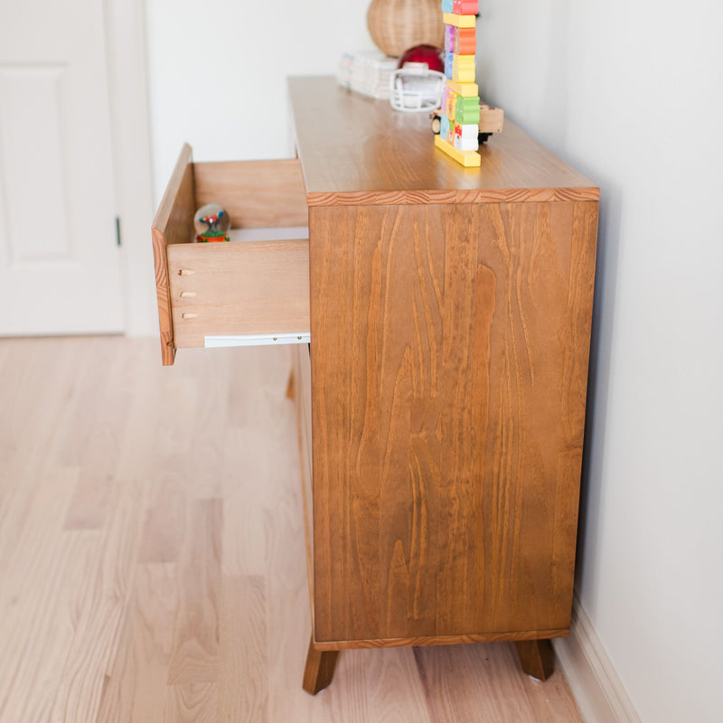 Mid-century modern wooden dresser with open drawer and colorful children's stacking toy on top in bright nursery with light hardwood floor and white walls