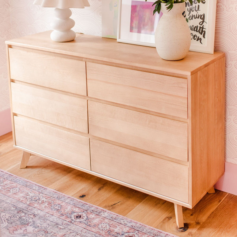 Modern Scandinavian light-wood six-drawer dresser on hardwood floor with ceramic vase, sculptural lamp, framed art and pink patterned rug