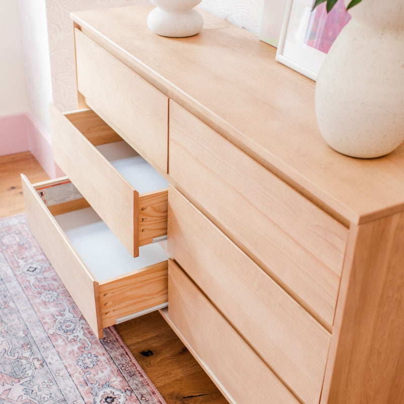 Light wood dresser with open drawers in a minimalist Scandinavian bedroom, ceramic vases on top and a pink patterned rug