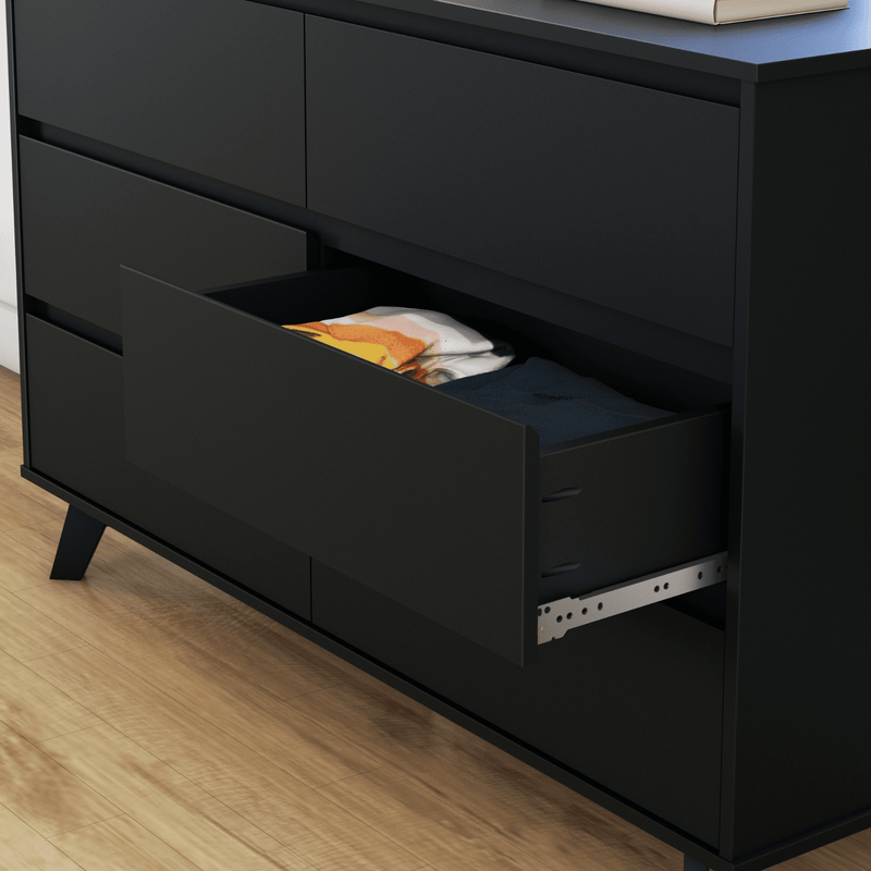 Matte black modern dresser with an open drawer revealing folded clothes and exposed metal drawer slide on light hardwood floor